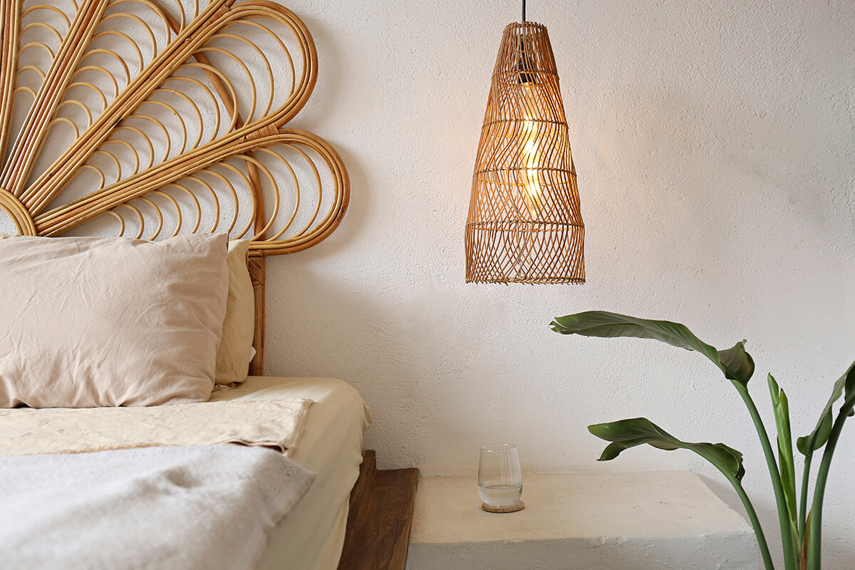 Bedroom with coastal interior design style, featuring rattan lights and headboard, white sheets, and a live plant