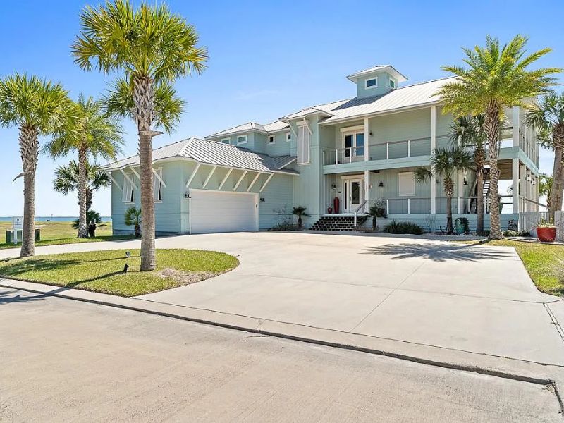 Exterior street-facing view of waterfront home with palm trees and sky blue paint scheme